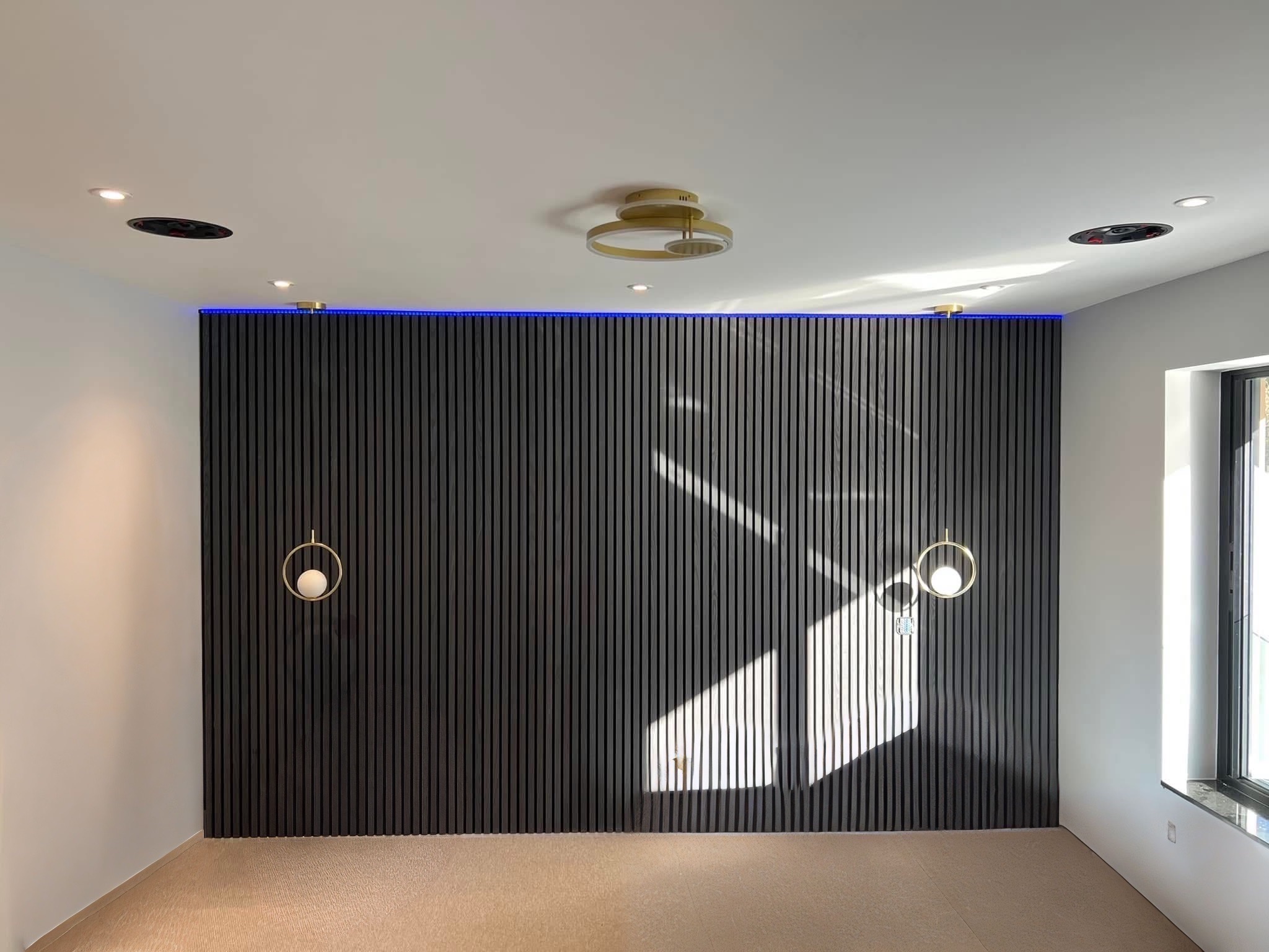A modern room designed by a skilled Basingstoke carpenter features a textured black feature wall, two circular pendant lights, ceiling lights, sunlight casting sharp patterns, and blue LED lighting along the top of the feature wall.